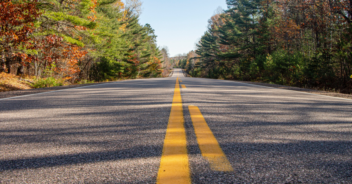 A picture of a paved road with green trees on either side.